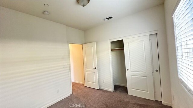 unfurnished bedroom with a closet, dark carpet, and multiple windows