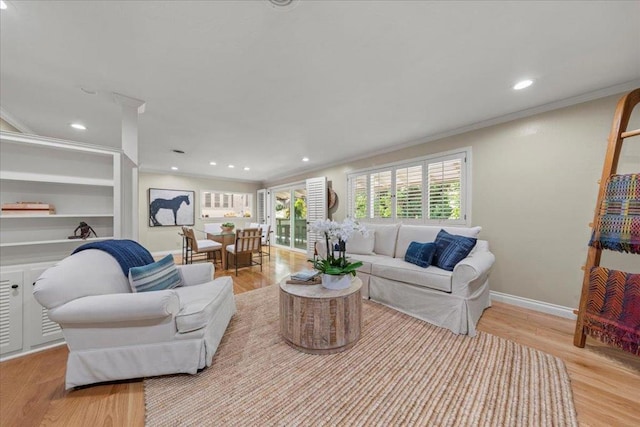 living room featuring crown molding, built in shelves, and light hardwood / wood-style flooring