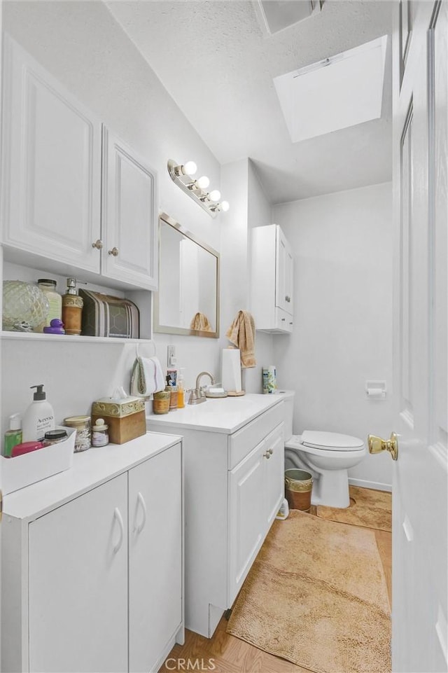 bathroom with a skylight, vanity, wood-type flooring, and toilet