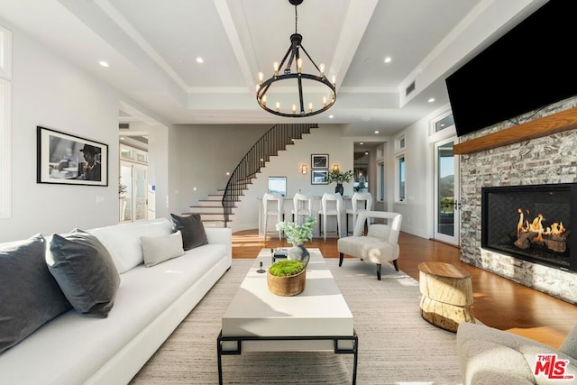 living room with a stone fireplace, a raised ceiling, light hardwood / wood-style floors, and a notable chandelier