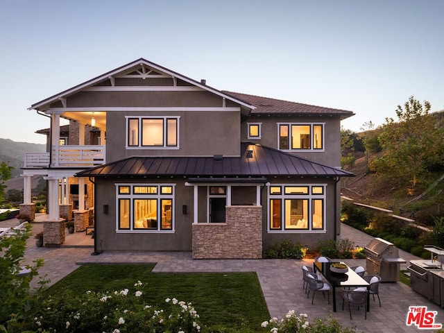 back house at dusk with a balcony, a lawn, and a patio area