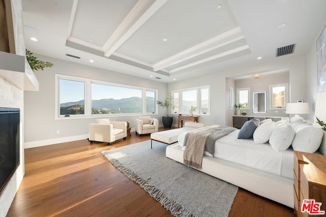 bedroom featuring wood-type flooring, multiple windows, and a raised ceiling