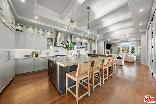 kitchen featuring decorative light fixtures, an island with sink, light stone countertops, and light wood-type flooring