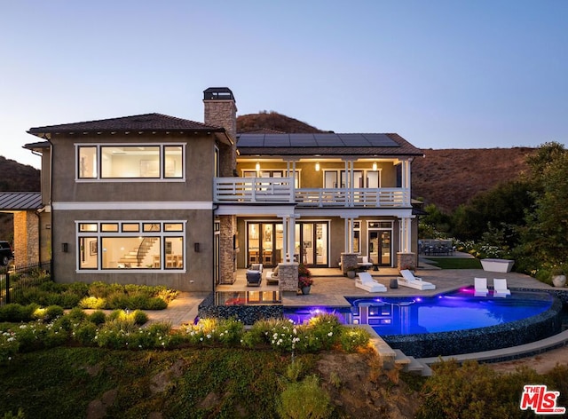 back house at dusk with a balcony, outdoor lounge area, solar panels, and a patio area