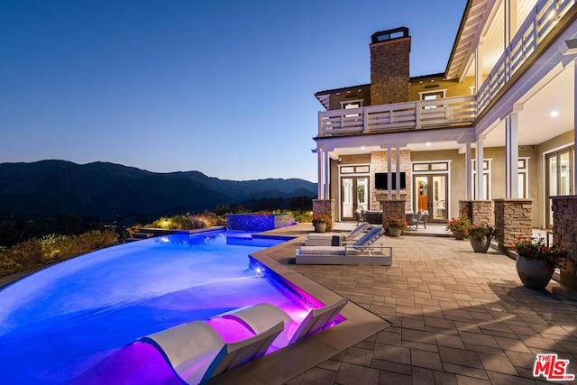 pool at dusk with french doors, a mountain view, a jacuzzi, and a patio area