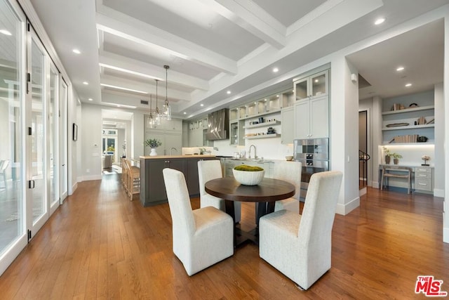 dining space with wood-type flooring, beam ceiling, an inviting chandelier, and sink