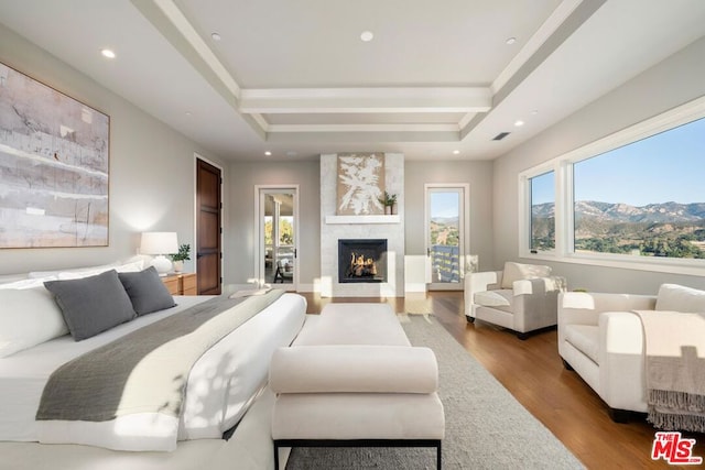 bedroom featuring wood-type flooring, a mountain view, a raised ceiling, and a fireplace