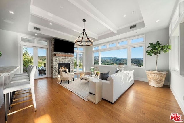 living room featuring light wood-type flooring, a stone fireplace, beam ceiling, and a notable chandelier