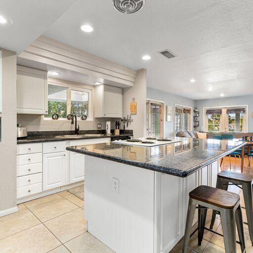 kitchen with a textured ceiling, sink, white cabinets, a kitchen bar, and light tile patterned floors