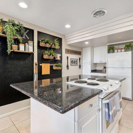 kitchen featuring white cabinetry, white appliances, light tile patterned floors, a center island, and dark stone counters