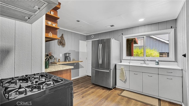 kitchen featuring range, sink, wooden walls, hardwood / wood-style floors, and stainless steel fridge