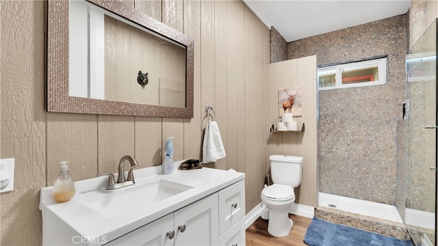 bathroom with a tile shower, wood walls, hardwood / wood-style floors, vanity, and toilet