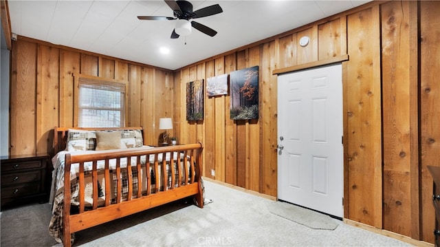 carpeted bedroom featuring ceiling fan and wooden walls