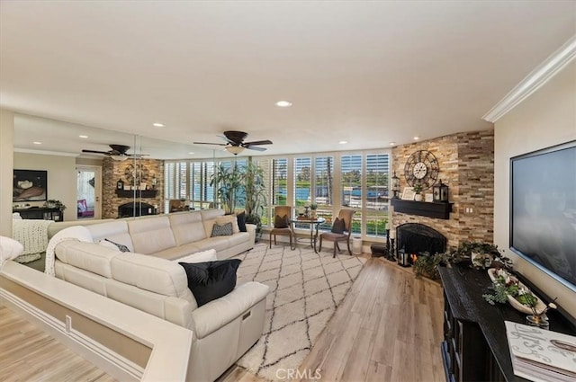 living room with crown molding, ceiling fan, a stone fireplace, and light hardwood / wood-style flooring