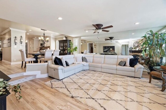 living room featuring ceiling fan with notable chandelier, ornamental molding, and light wood-type flooring