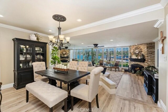 dining area with floor to ceiling windows, ceiling fan with notable chandelier, a fireplace, and light hardwood / wood-style flooring