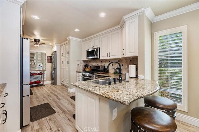 kitchen with sink, ceiling fan, white cabinetry, stainless steel appliances, and light stone countertops