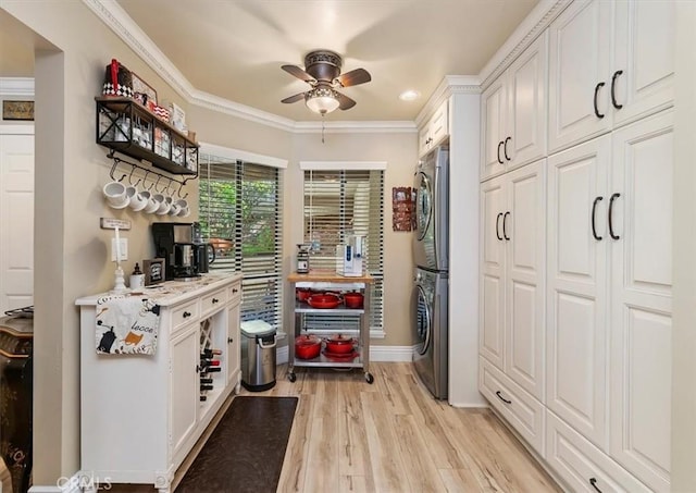 kitchen with crown molding, ceiling fan, stacked washing maching and dryer, white cabinetry, and light hardwood / wood-style floors