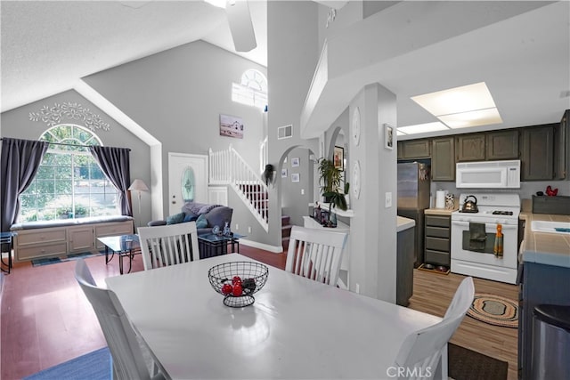 dining space with light hardwood / wood-style floors, ceiling fan, and high vaulted ceiling