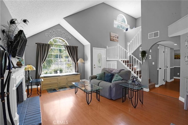 living room with wood-type flooring, a textured ceiling, a fireplace, and high vaulted ceiling