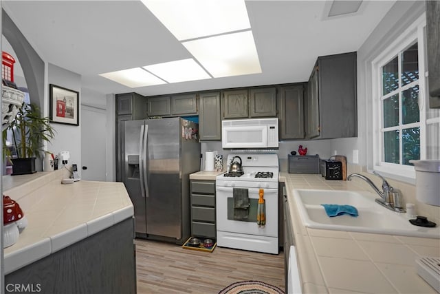 kitchen with sink, light wood-type flooring, tile counters, and white appliances