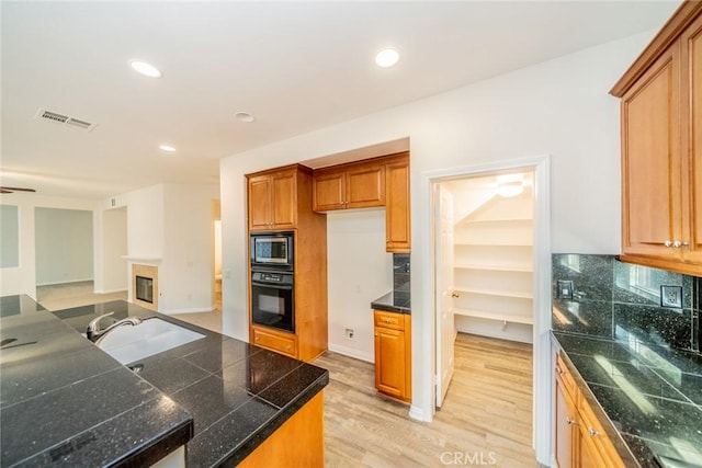 kitchen with visible vents, tile countertops, stainless steel microwave, a sink, and black oven