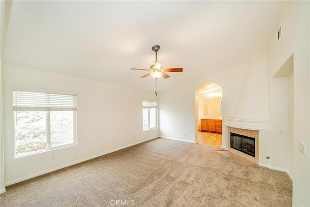 unfurnished living room with arched walkways, light colored carpet, a large fireplace, ceiling fan, and baseboards