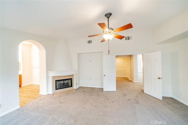 unfurnished living room with light carpet, a fireplace, visible vents, and arched walkways