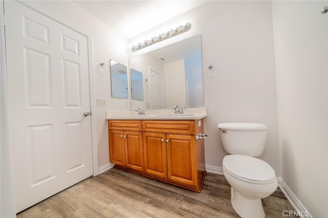 bathroom with double vanity, toilet, a sink, wood finished floors, and baseboards