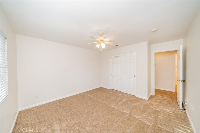 unfurnished bedroom with a closet, visible vents, a ceiling fan, light carpet, and baseboards