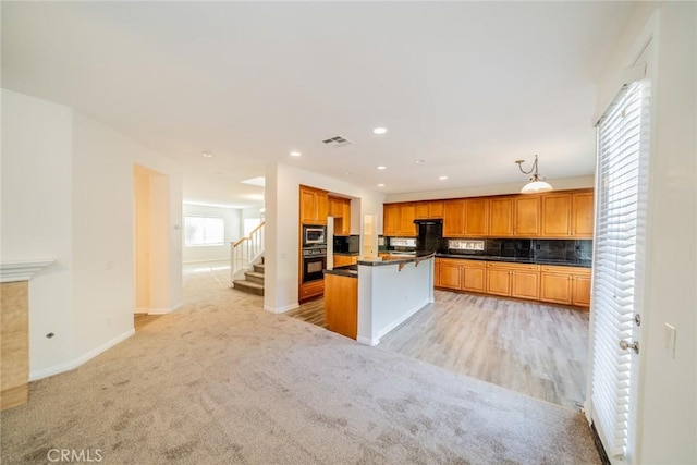 kitchen with dark countertops, stainless steel microwave, visible vents, decorative backsplash, and light carpet