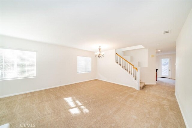 unfurnished living room featuring a chandelier, light colored carpet, and plenty of natural light