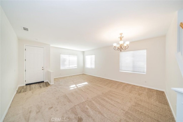 unfurnished room with light colored carpet, baseboards, and an inviting chandelier