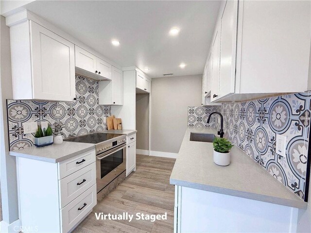 kitchen with light wood-style flooring, high end stove, a sink, light countertops, and backsplash
