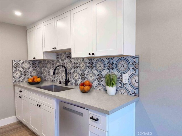 kitchen with tasteful backsplash, dishwasher, light countertops, white cabinets, and a sink