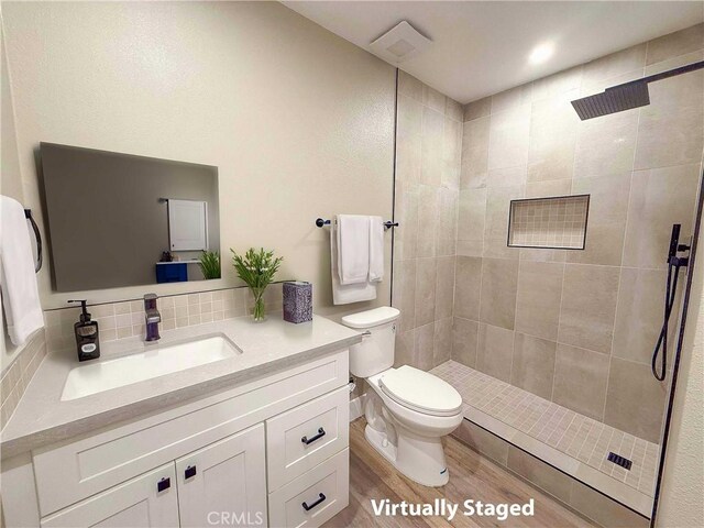 full bath featuring toilet, a tile shower, decorative backsplash, wood finished floors, and vanity