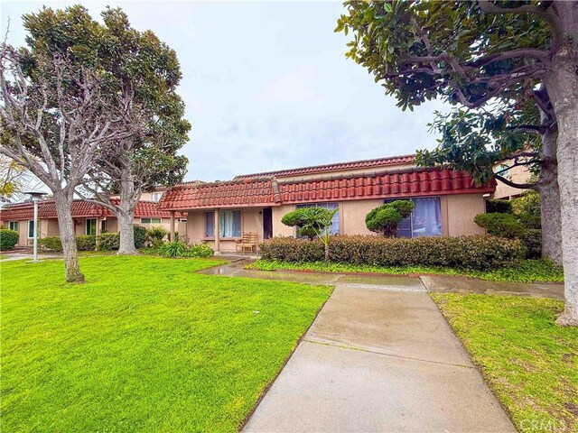 view of front of house with stucco siding, a front yard, and a tiled roof
