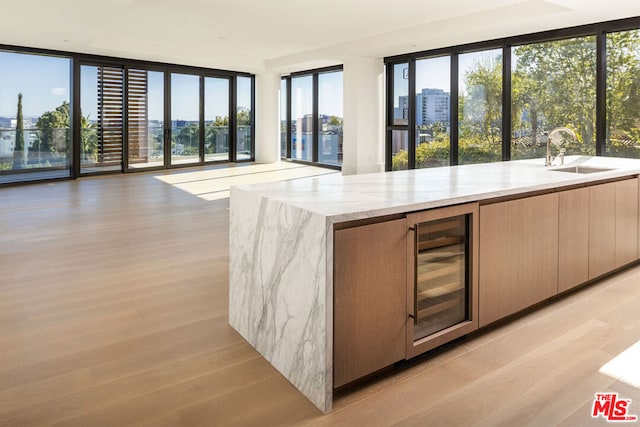 kitchen with sink, beverage cooler, light stone countertops, floor to ceiling windows, and light hardwood / wood-style floors