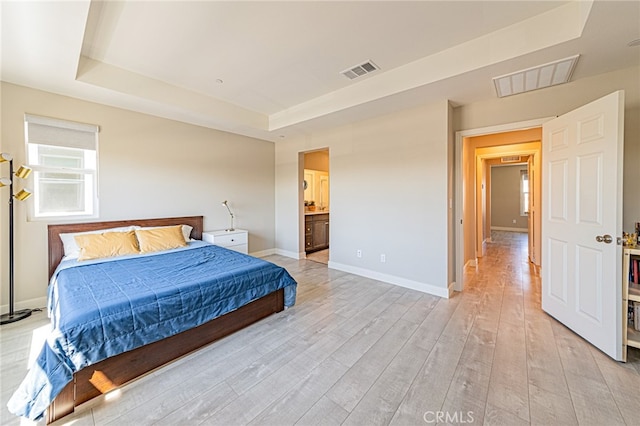 bedroom featuring light hardwood / wood-style flooring, ensuite bathroom, and a tray ceiling