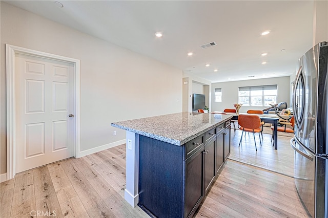 kitchen featuring light stone counters, light hardwood / wood-style floors, a center island, and stainless steel refrigerator