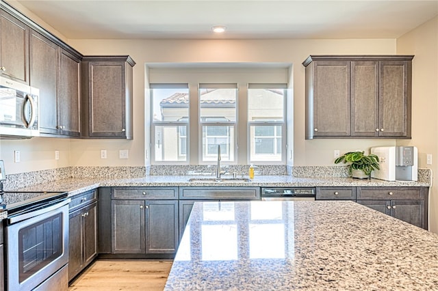 kitchen with dark brown cabinets, light hardwood / wood-style floors, sink, appliances with stainless steel finishes, and light stone countertops