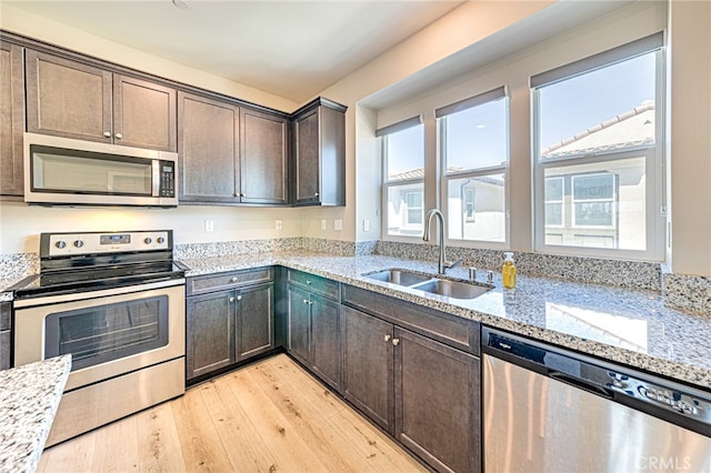 kitchen with light hardwood / wood-style flooring, light stone counters, appliances with stainless steel finishes, and sink