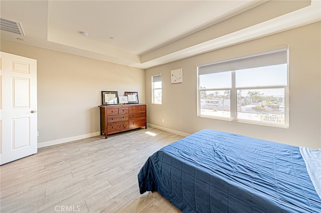 bedroom with light hardwood / wood-style flooring and a raised ceiling