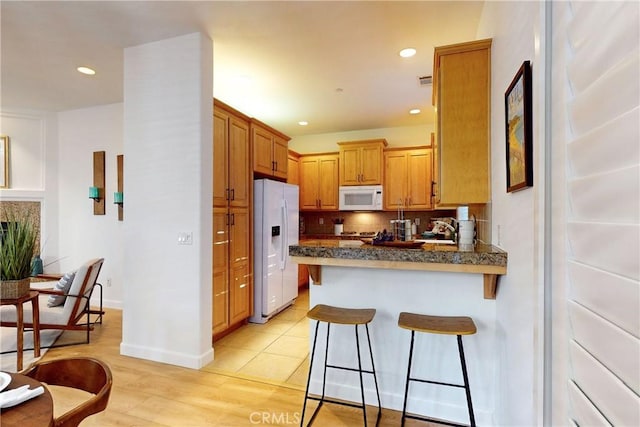 kitchen with white appliances, a kitchen breakfast bar, decorative backsplash, light wood-type flooring, and kitchen peninsula