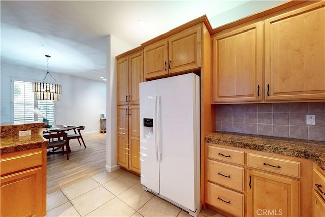 kitchen with white fridge with ice dispenser, hanging light fixtures, an inviting chandelier, tasteful backsplash, and light tile patterned floors