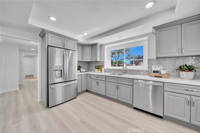 kitchen with light hardwood / wood-style floors, sink, stainless steel appliances, and a tray ceiling