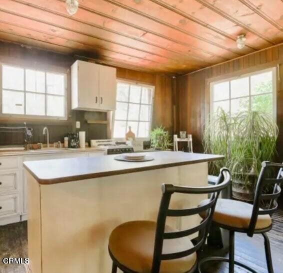 kitchen featuring white cabinets, a center island, wooden ceiling, and wooden walls