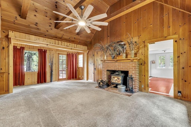 unfurnished living room featuring a healthy amount of sunlight, carpet, beamed ceiling, and a wood stove