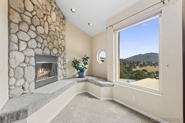 living area with light carpet, a stone fireplace, a mountain view, and lofted ceiling