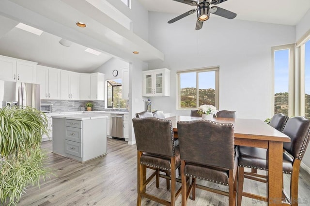 dining space with high vaulted ceiling, ceiling fan, light hardwood / wood-style flooring, and sink